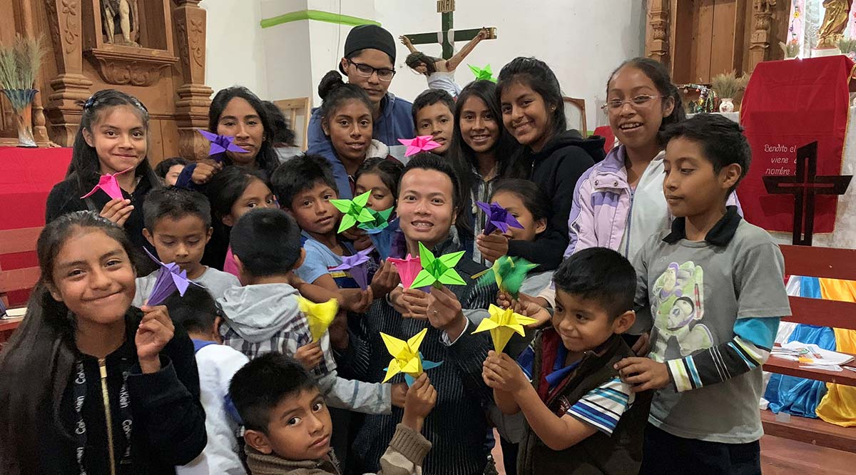 Derek Nguyen is surrounded by children in a church holding paper flowers