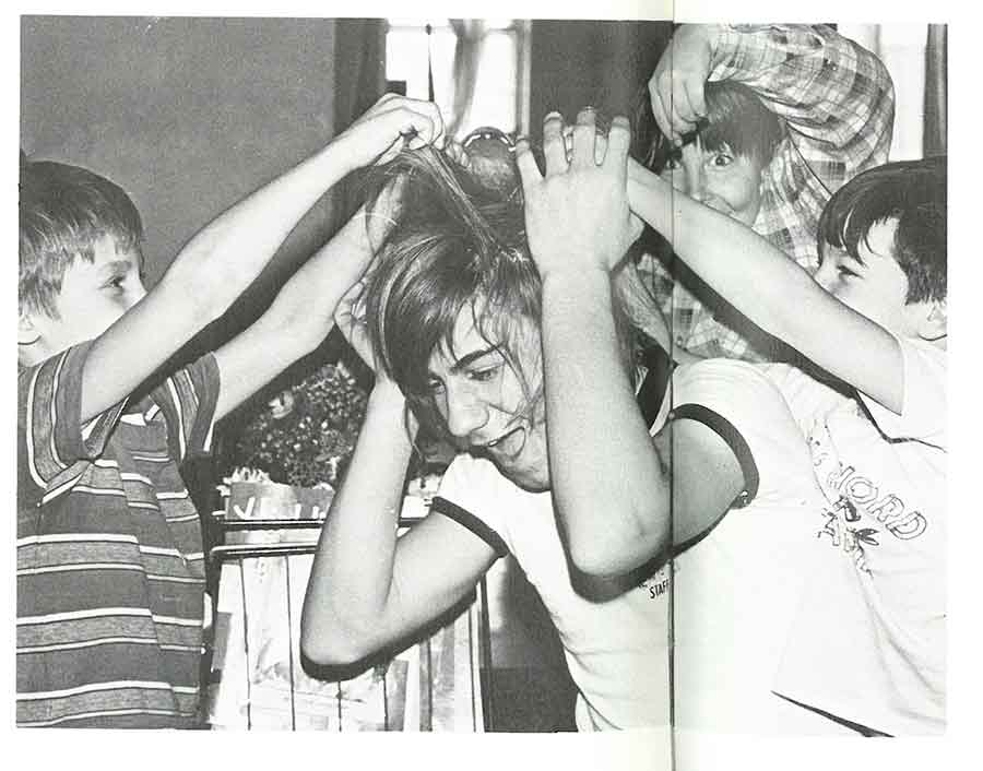 Elementary age boys mess the hair of a high school boy in black and white photo